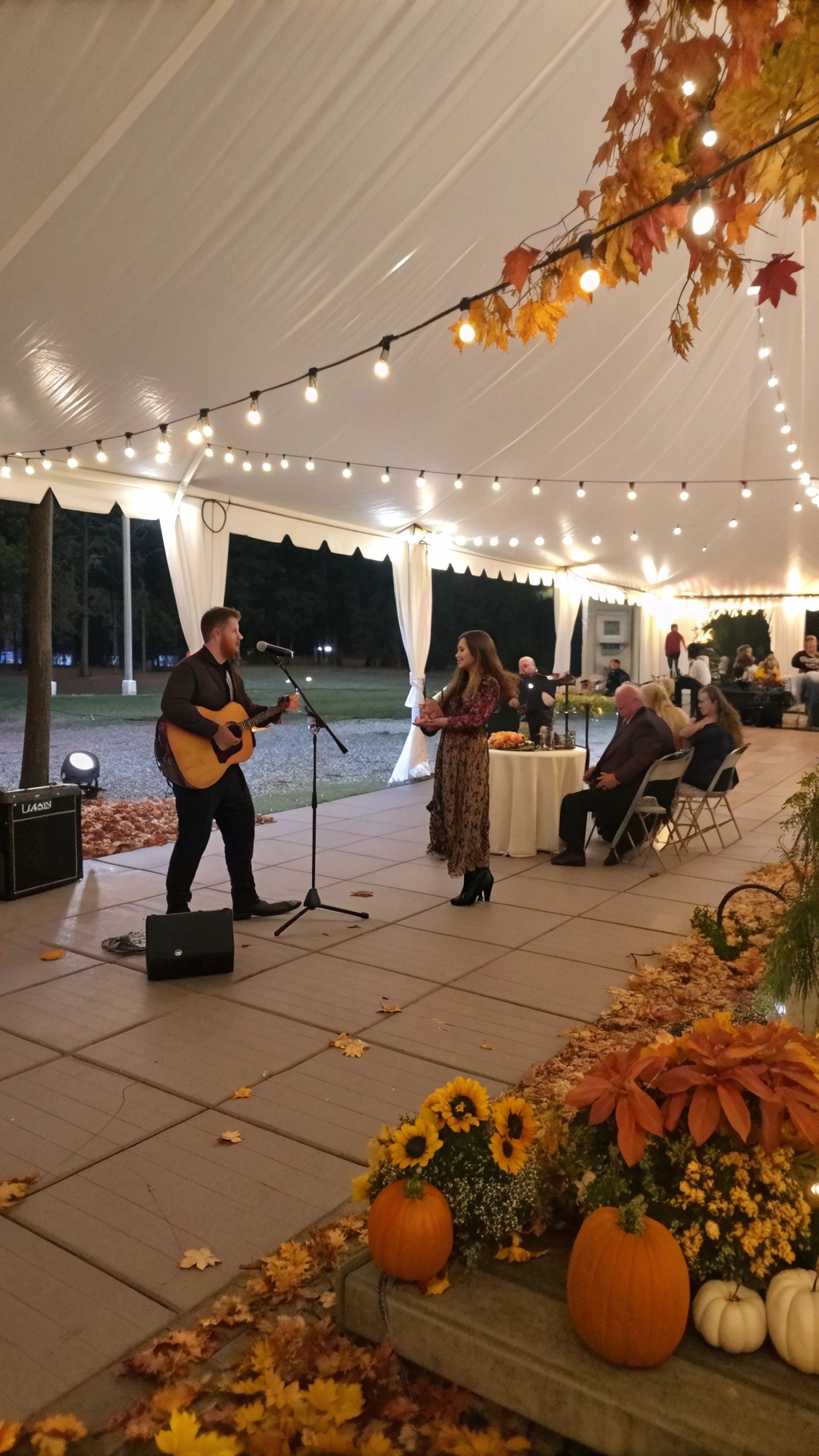 A musician performing with a guitar under a tent decorated with fall leaves and pumpkins.